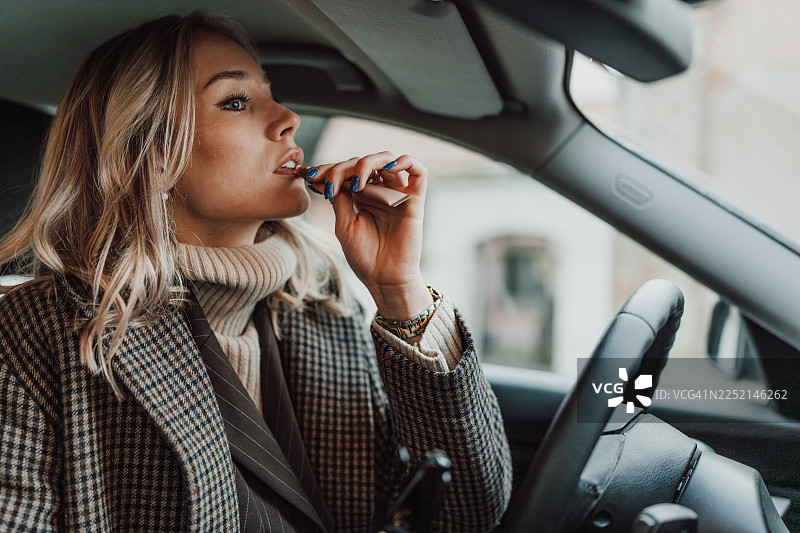 坐着方向盘后，正在涂抹口红的时尚女性图片素材