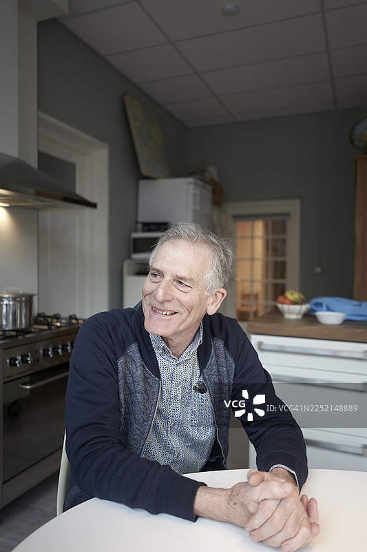 面带微笑的男人坐在厨房的餐桌旁，看向一旁图片素材