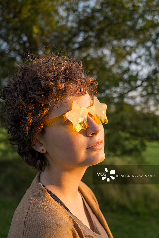 公园里，夕阳下，戴着星星眼镜的年轻人的肖像图片素材