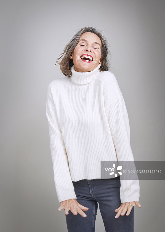 身穿高领毛衣、留着灰发、面带微笑的女性，工作室肖像照图片素材