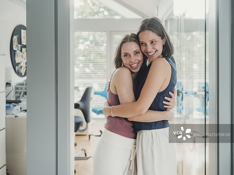 在现代家庭办公室环境中，女性互相拥抱并微笑图片素材