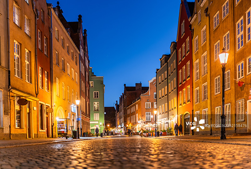 傍晚时分，在格但斯克老城的鹅卵石街道上，低角度拍摄的色彩缤纷的公寓楼和街灯。图片素材