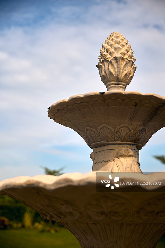 一座古典花园喷泉，采用分层设计，顶部饰有松果，在湛蓝的天空映衬下显得格外醒目。图片素材