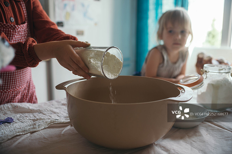 孩子在家里的厨房里，和朋友一起烘焙，往碗里倒面粉图片素材