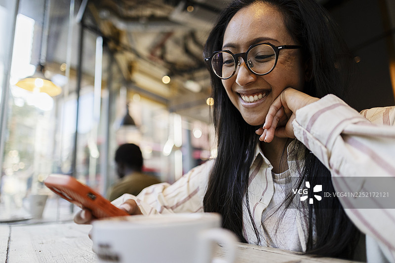 戴眼镜的女士在咖啡店里微笑着使用智能手机图片素材
