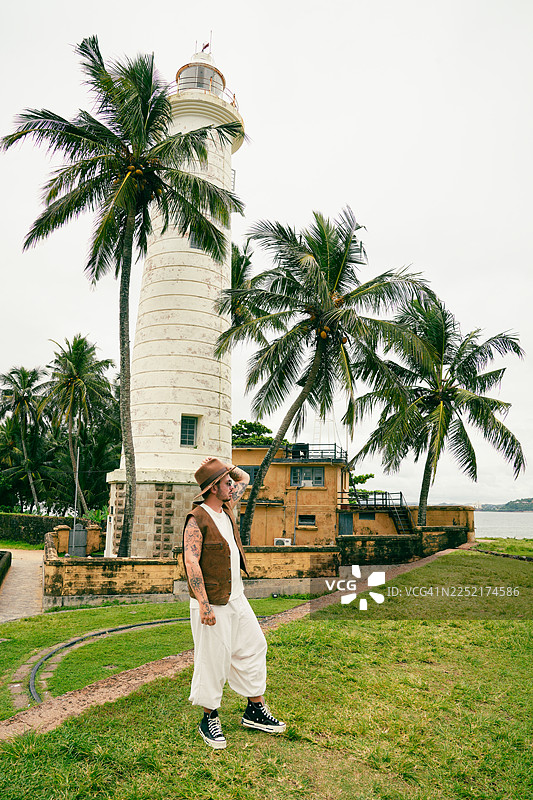 一位穿着棕色麂皮背心和帽子的时尚男士在斯里兰卡加勒灯塔前摆姿势图片素材