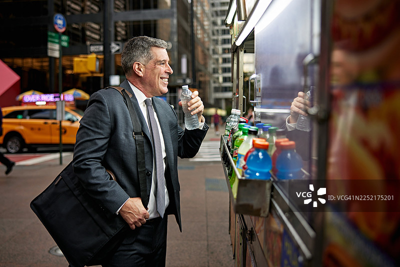 一位成熟的商界男士在纽约街头食品车购买瓶装水图片素材