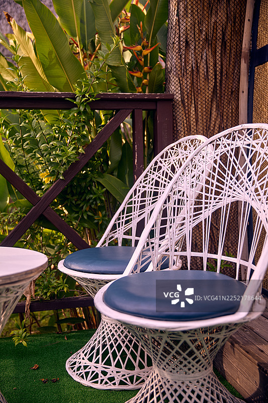 两个带蓝色坐垫的白色编织椅摆放在小小的户外露台上。图片素材