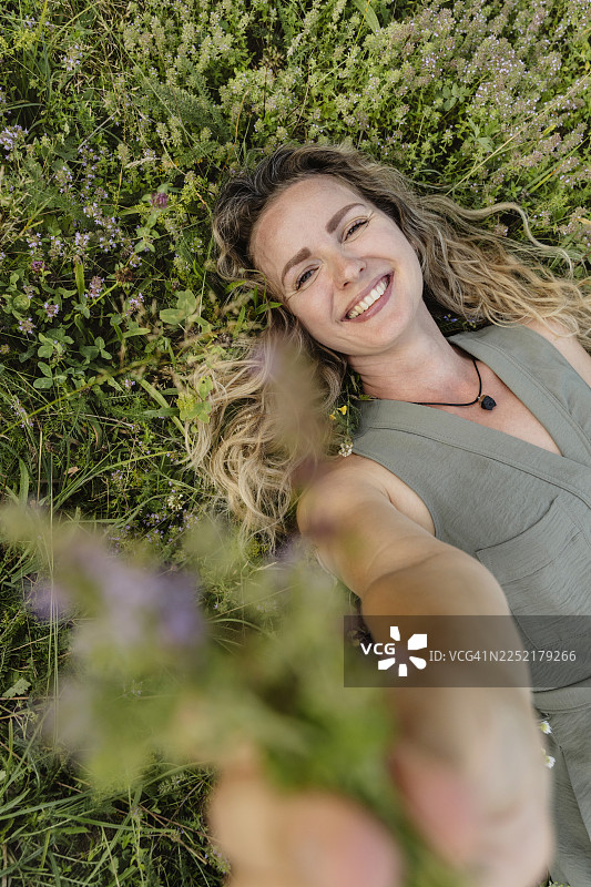 一位女士微笑着在草地上采集香草香料，享受户外时光图片素材