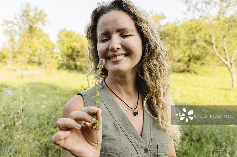 面带微笑的女子在户外自然环境中手持野生香草，享受芳香疗法图片素材