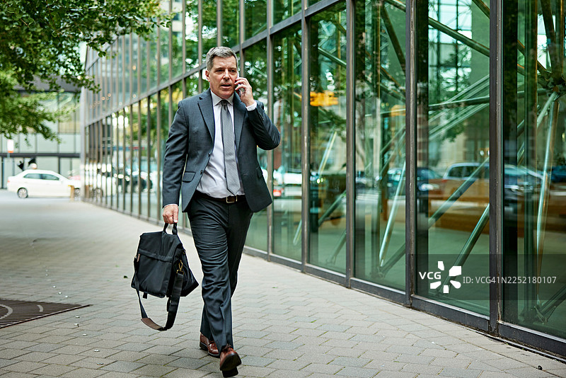 商务人士在城市街道上边走边打电话图片素材