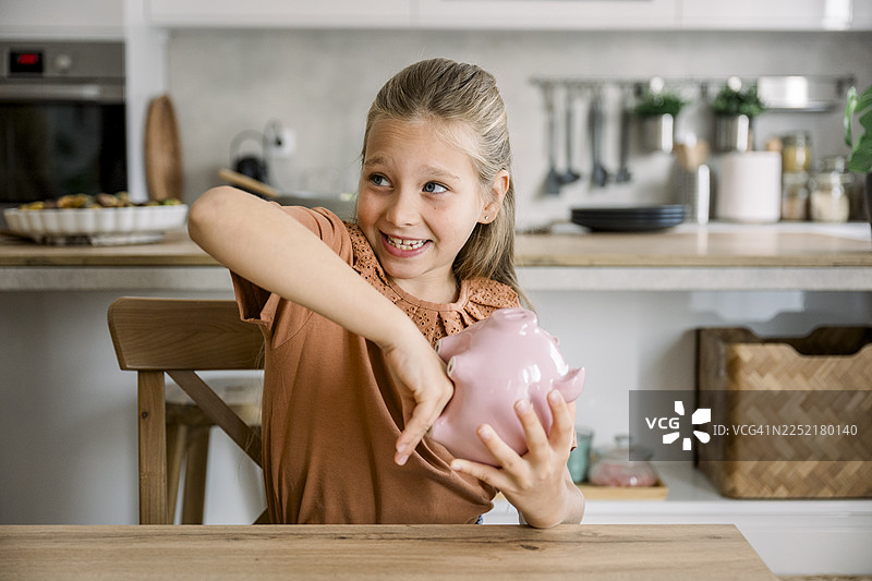 快乐的女孩在家里的厨房里往储蓄罐里存钱图片素材