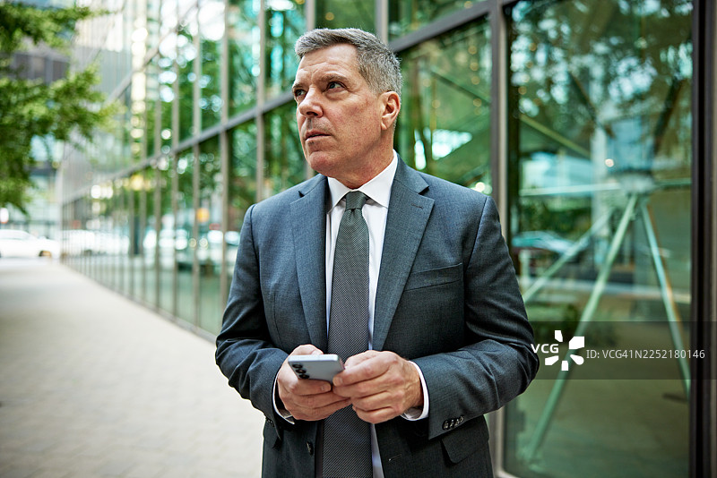 商务人士站在办公楼外，手中拿着手机图片素材