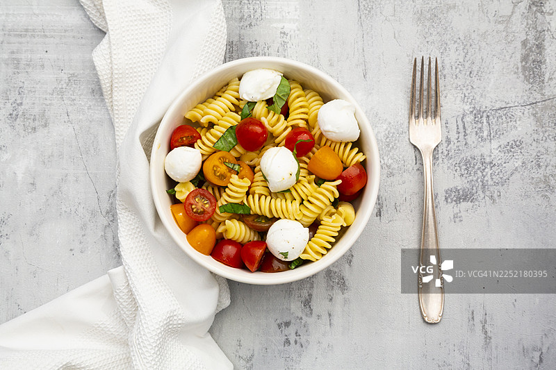 罗勒番茄马苏里拉奶酪意面沙拉盛放在灰色水泥板上图片素材