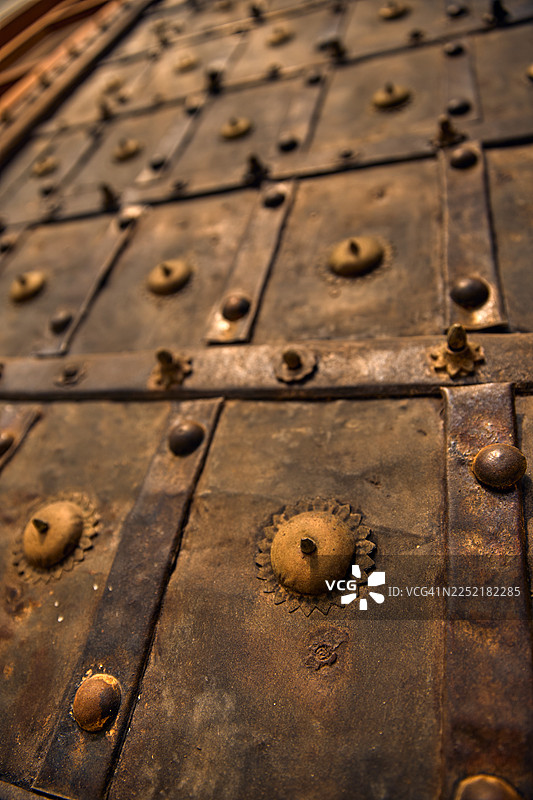 一扇带有金属加固、铆钉和做旧纹理表面的结实木门特写。图片素材