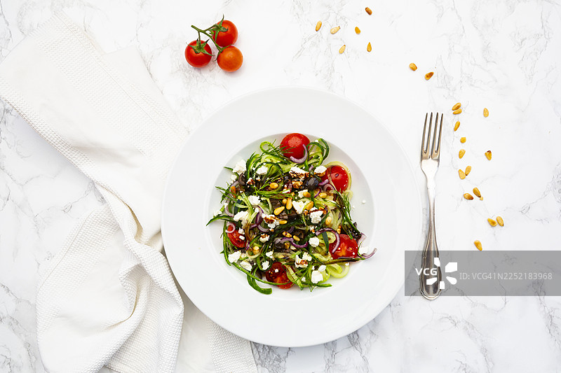 黄瓜沙拉配菲达奶酪、圣女果、橄榄和松子，放在大理石上图片素材