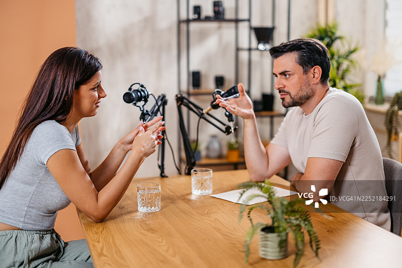 播客节目中，一位男主持人与一位女嘉宾在录音棚里对着麦克风交谈图片素材