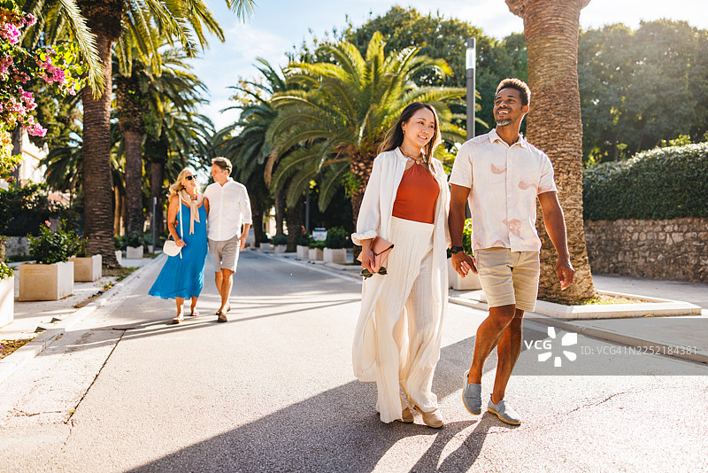 一对快乐的情侣漫步在棕榈树成荫的达尔马提亚街道上图片素材