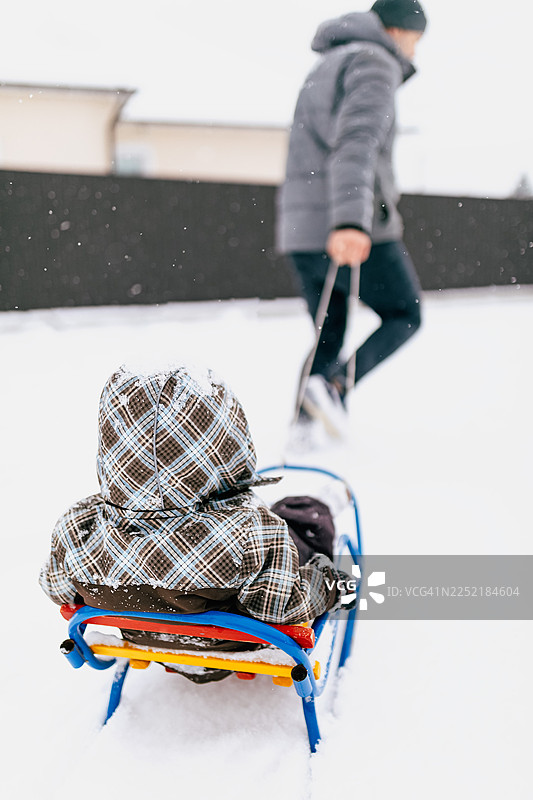 父亲在雪天户外拉着孩子坐雪橇，享受冬日雪景图片素材