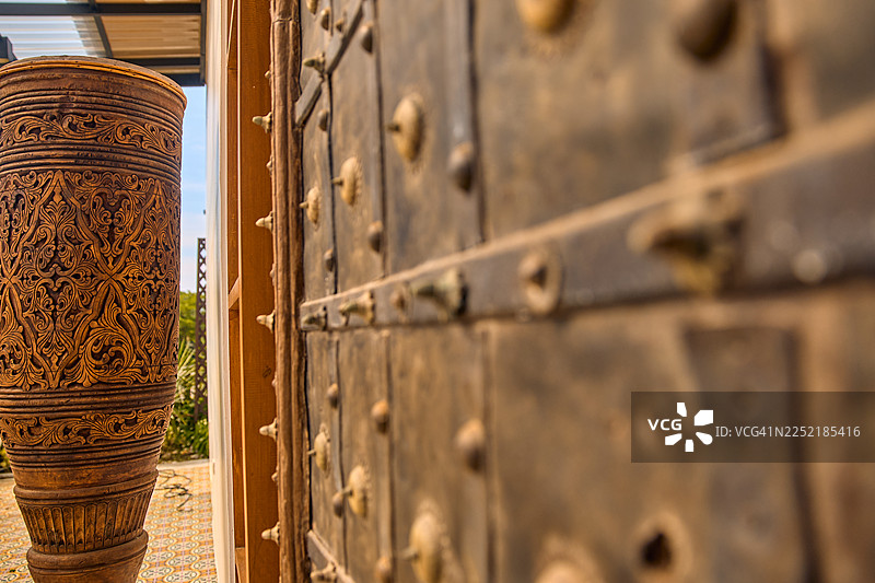 特写镜头，对比了雕刻的木制物品和布满铆钉的做旧金属门。图片素材