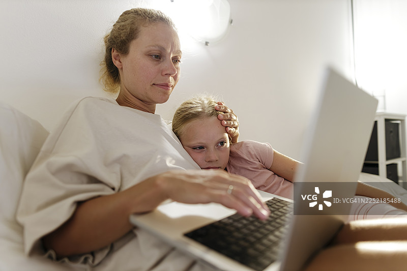 妈妈在笔记本电脑上工作，生病的孩子依偎在身边寻求安慰图片素材