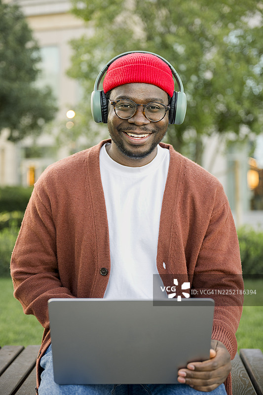 戴着耳机、面带微笑的男士坐在户外，使用笔记本电脑进行视频通话图片素材