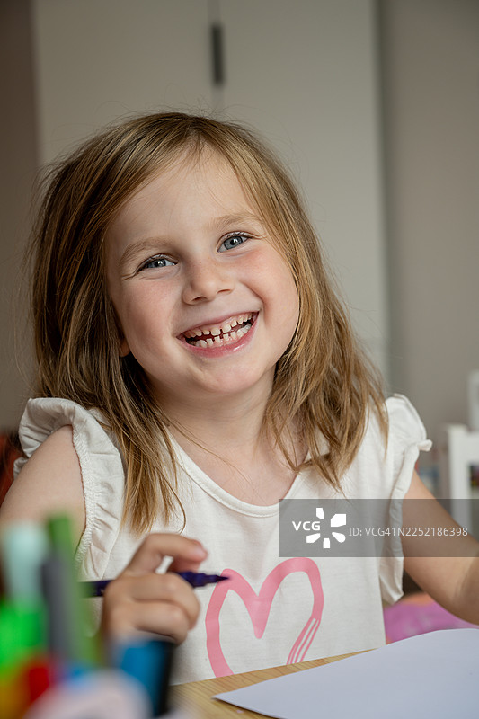 室内创意活动中，一个孩子微笑着在书桌前绘画图片素材