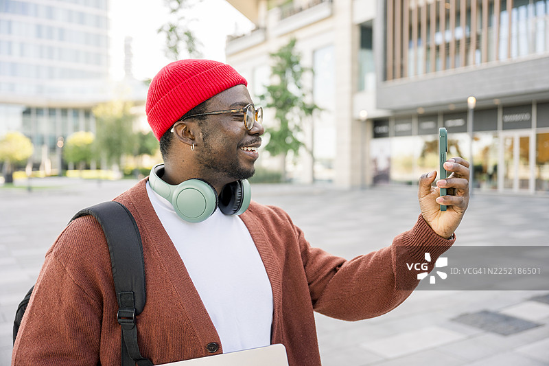 城市背景下，一位男士正微笑着使用智能手机拍照图片素材