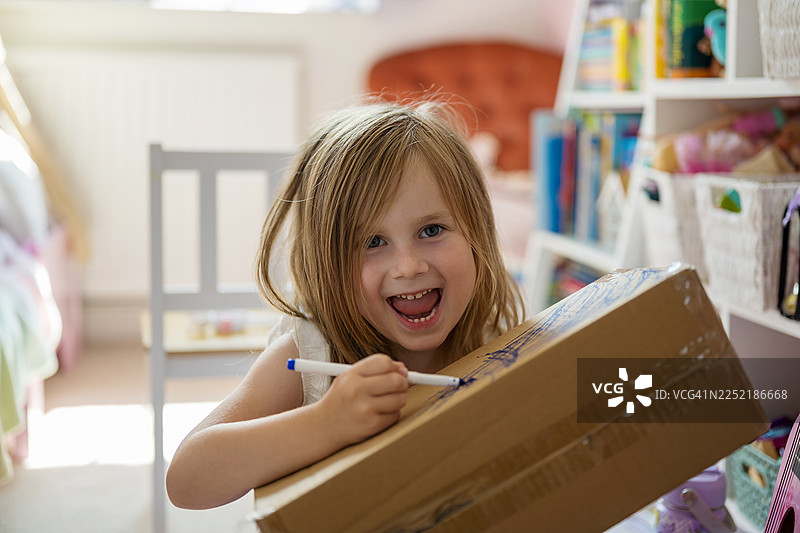 孩子在创意活动中，一边笑着一边在纸板箱上画画图片素材