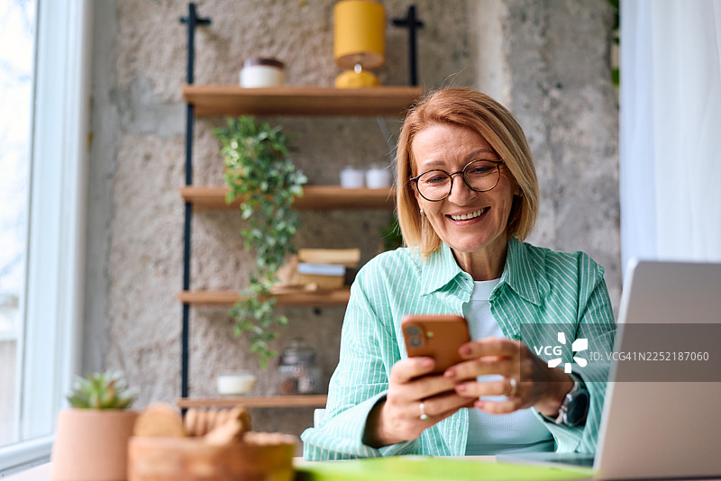 快乐的成熟的女性在家中使用智能手机图片素材