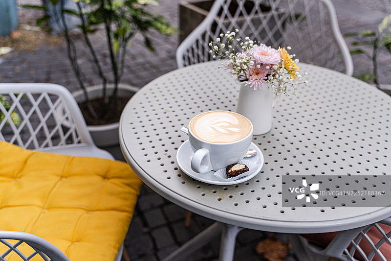 花园桌上的卡布奇诺咖啡和酿有香橙辣味黄油的椰枣，旁边还有一束鲜花图片素材