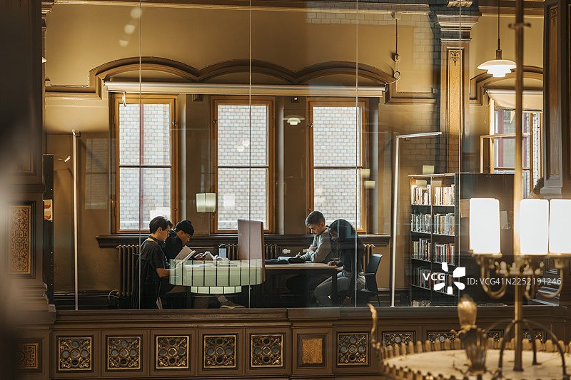 透过玻璃墙看到的大学图书馆里正在学习的成年学生图片素材