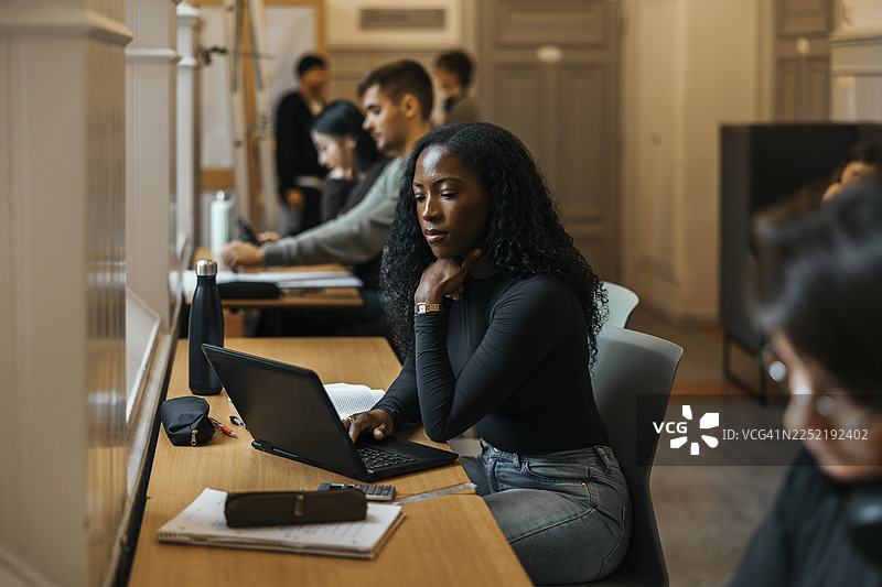 年轻女子在大学图书馆的桌子前专注地使用笔记本电脑学习图片素材