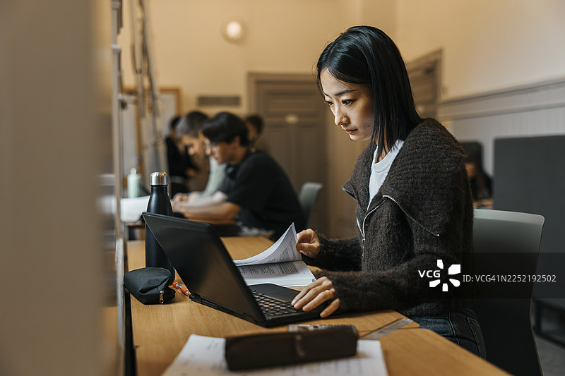 女大学生在大学图书馆用笔记本电脑和书本专注学习图片素材