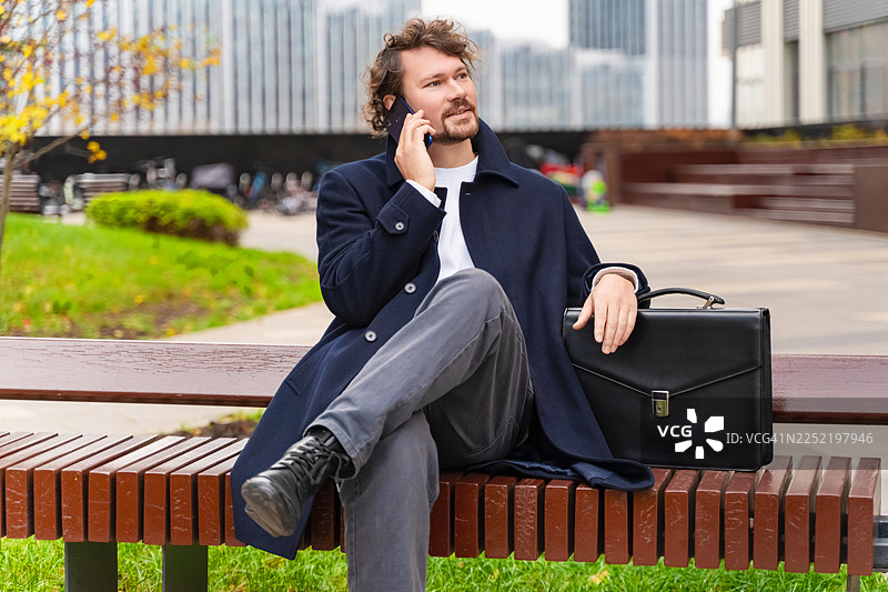 城市公园背景下，穿着外套的男子坐在长椅上进行商务谈话图片素材