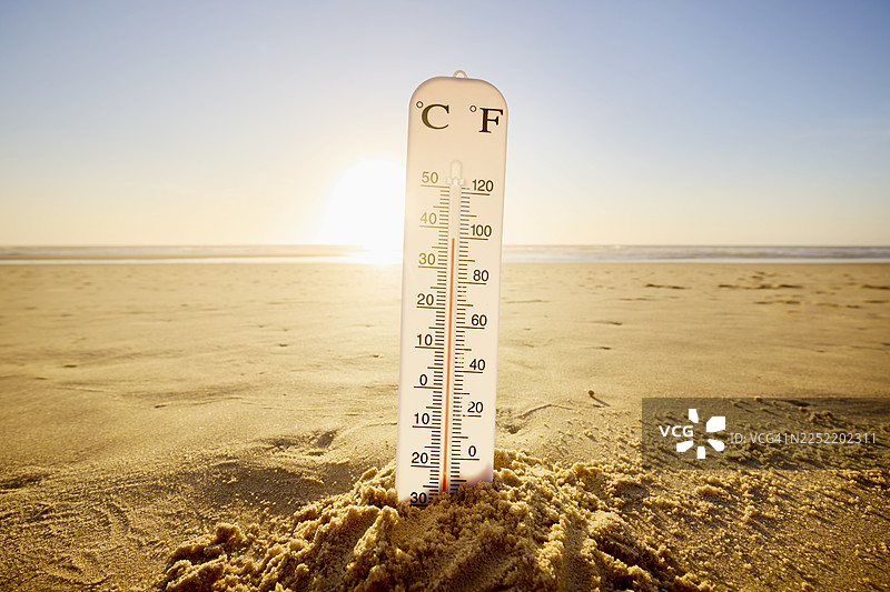 沙滩上的沙堡插着温度计，背景是太阳、大海和天空图片素材