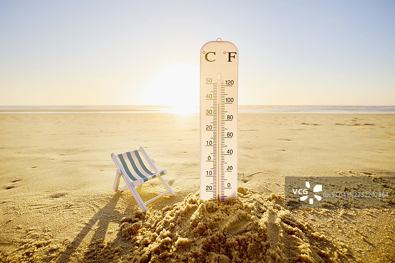 沙滩上的温度计和沙堡旁的折叠椅，背景是阳光、大海和天空图片素材