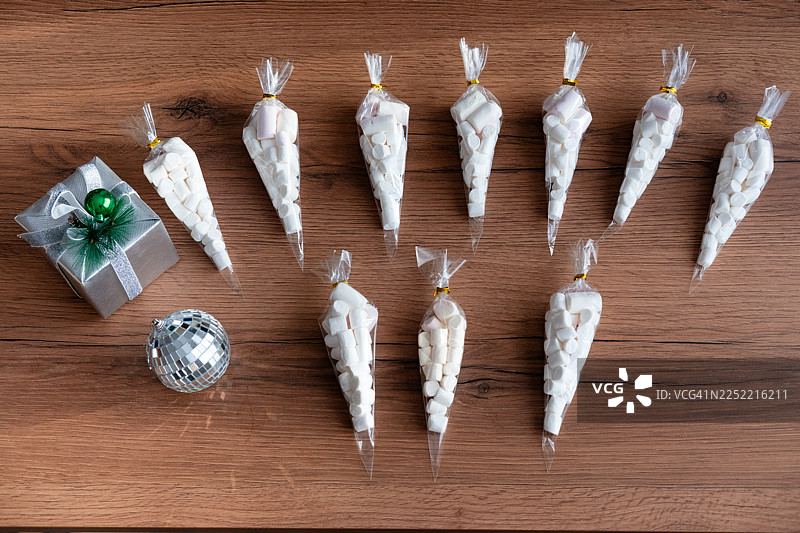 木质背景上装有棉花糖的小礼品袋和节日礼盒，适合作为甜蜜的礼物。图片素材