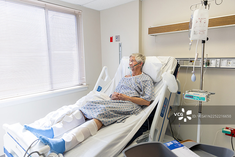 一位年长的男士躺在病床上，他的妻子在一旁照料支持他图片素材
