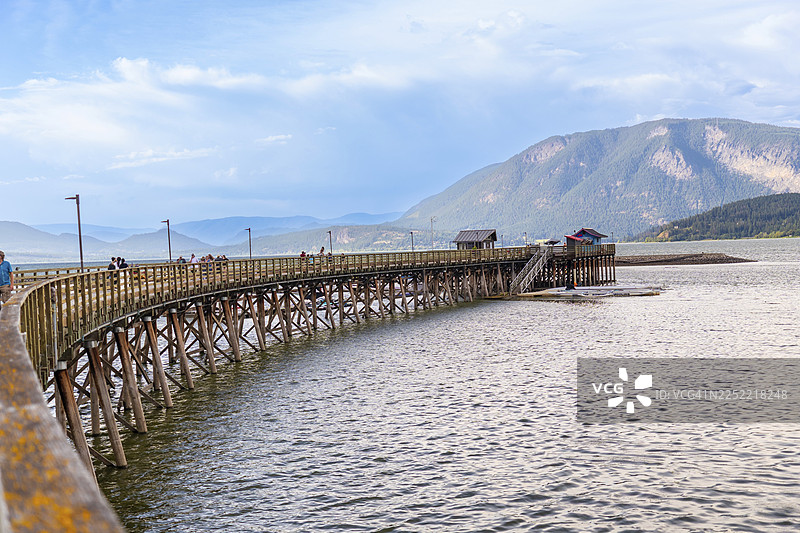 游客们在加拿大不列颠哥伦比亚省萨蒙阿姆市，北美最长的木制码头上享受着晴朗的一天，背景是连绵的山脉。图片素材
