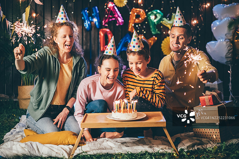 一个幸福的家庭，有两个孩子，在夜晚的户外庆祝生日，有蛋糕和仙女棒。图片素材