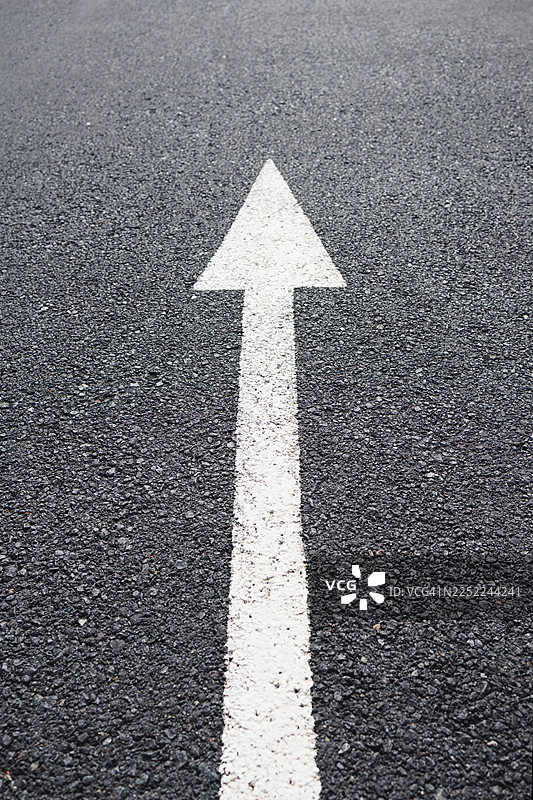 白色方向箭头漆在深色沥青路面上，指示前进方向和导航概念，交通标志标线表示单行道或直行图片素材