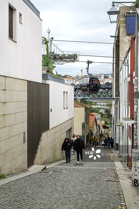 加亚缆车从波尔图一条狭窄街道上方经过，行人正在街道上行走图片素材