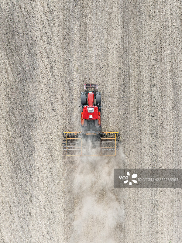红色拖拉机在尘土飞扬的田野里拖着一辆耕作机，从无人机视角拍摄，地点是英国斯塔福德郡。图片素材