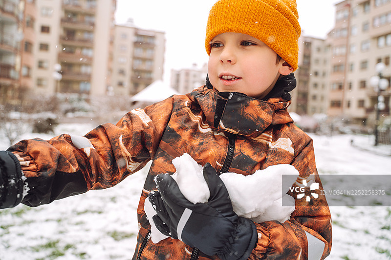 冬天，一个小男孩在院子里玩雪球图片素材