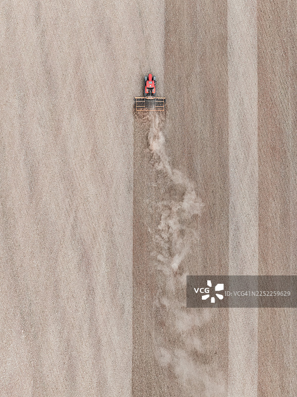 俯视画面，显示一辆红色的拖拉机在夏天耕作英格兰，联合王国，米德兰兹的干涸田野。图片素材