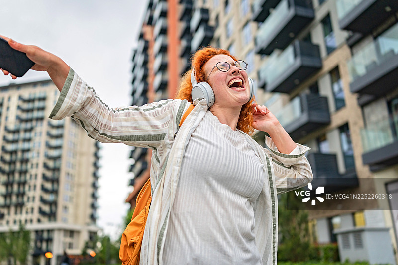 姜黄色头发的女士在阴天漫步城市，享受音乐和乐趣图片素材