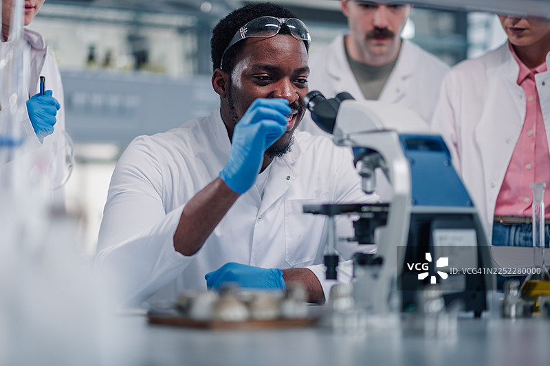 不同背景的科学家们在实验室里用显微镜进行研究图片素材