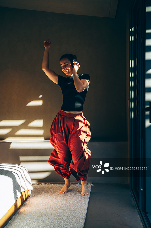 年轻女子在家中阳光下戴着耳机跳舞。赤脚微笑，穿着休闲服饰，在现代明亮的房间里享受音乐。图片素材