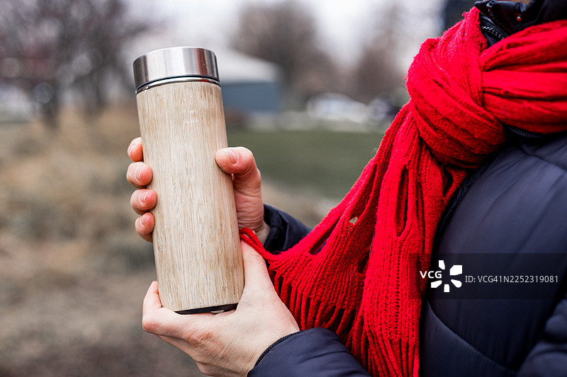 一个人在户外拿着木制保温杯，戴着红围巾，穿着冬装外套图片素材